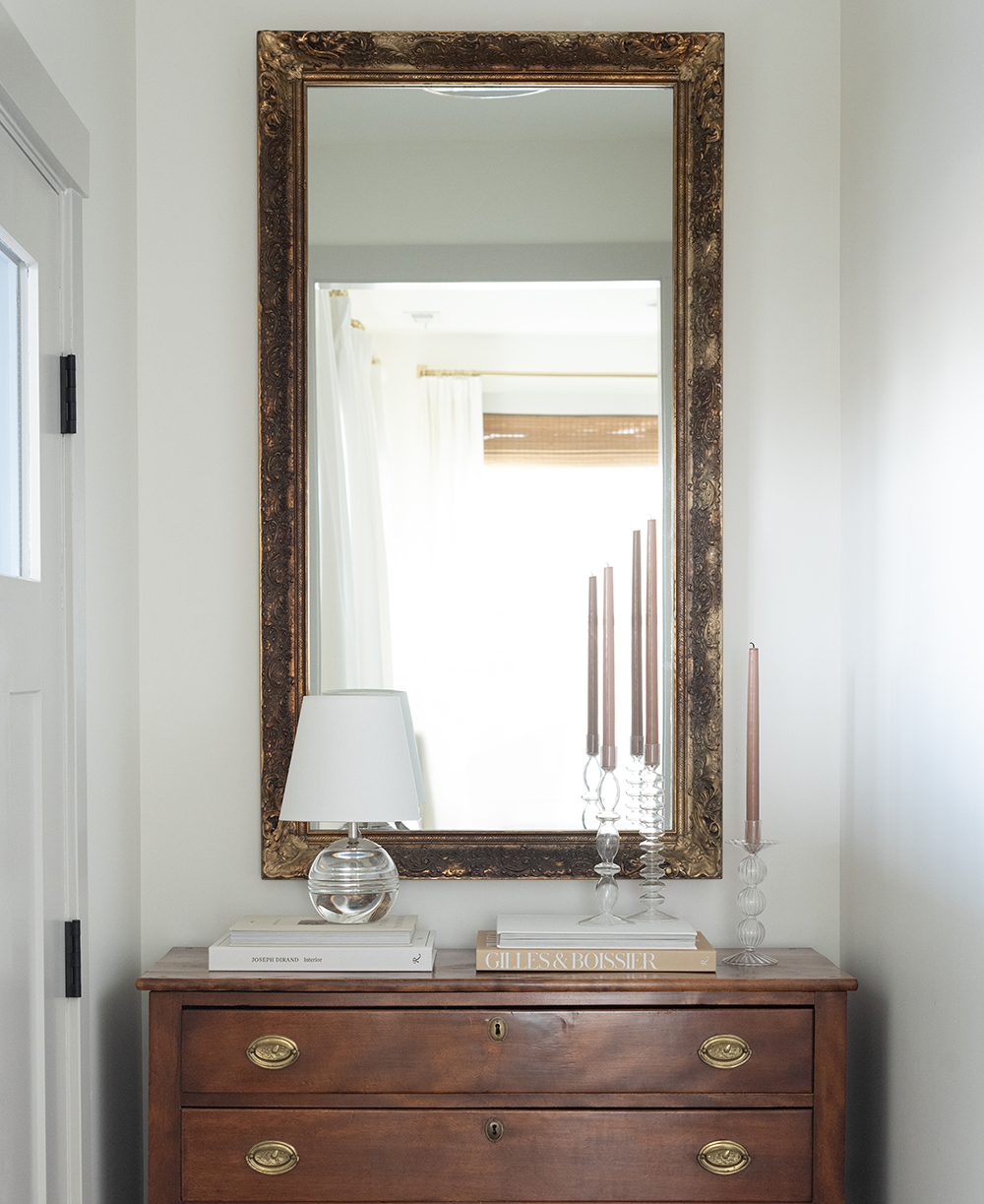 small entryway with a vintage dresser styled with a gold mirror, glass candleholders and crystal lamp.